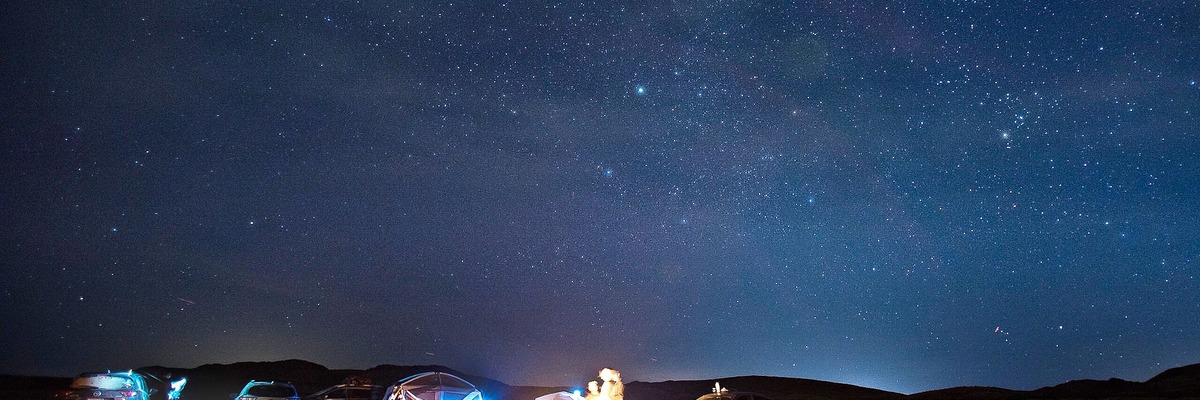 A 1200×400 center crop of the desert photo showing mostly sky, with the campsite cut off at the bottom edge.