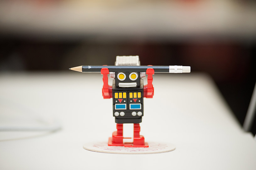 A photo of a toy robot holding a pencil above its head.
