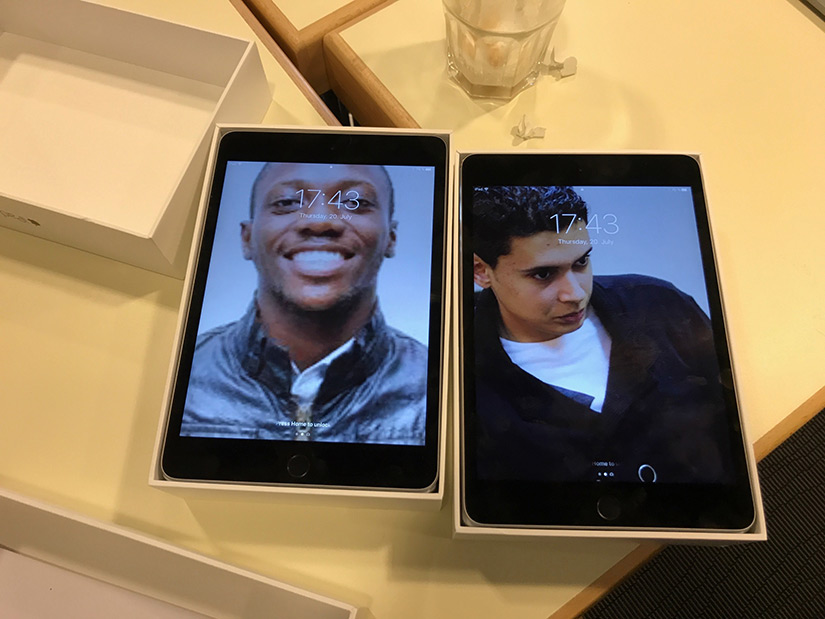 Two iPads with the lockscreens set to photos of the missing team members, Ife and Abdel.