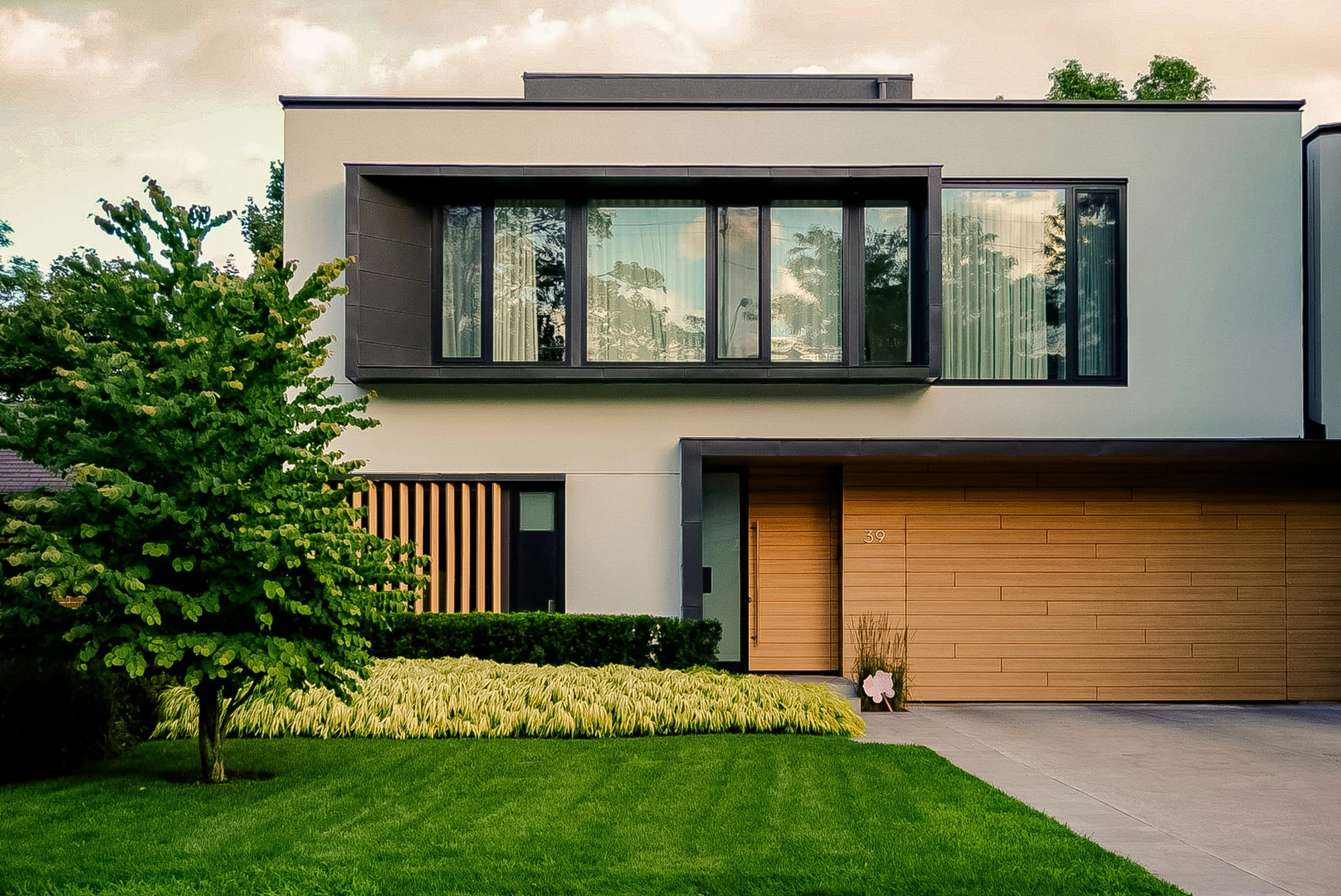 Une maison moderne de deux niveaux avec une pelouse à l’avant et une porte de garage en bois